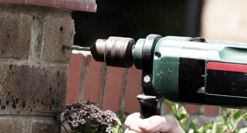 A homeowner drilling pilot holes into a small garden brick wall