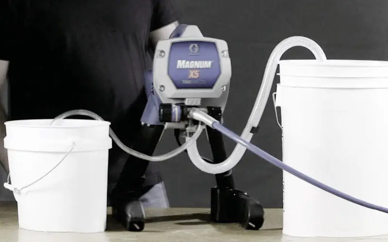 An image showing an airless paint sprayer system being flushed into buckets